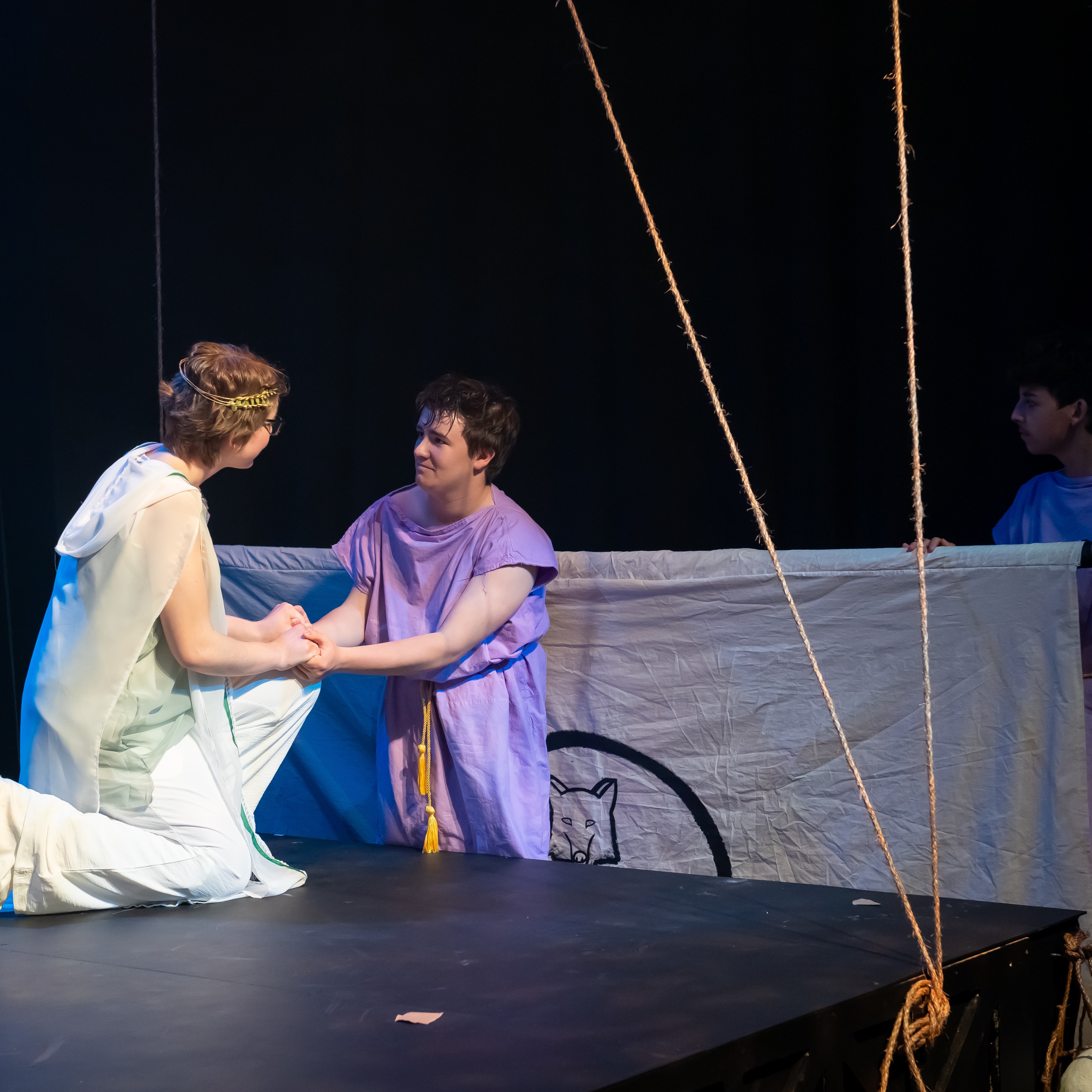 A young man in a purple robe is centered, he holds the hands of a woman in a white robe. Another man prepares to raise a white sail on the right.